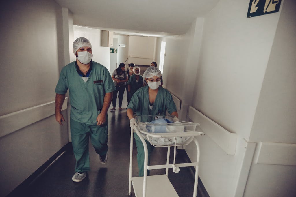 Unrecognizable obstetrician and nurse carrying newborn baby trolley in hospital